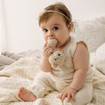 Baby in a cream outfit holding a plush toy on a braided Merino wool baby blanket.