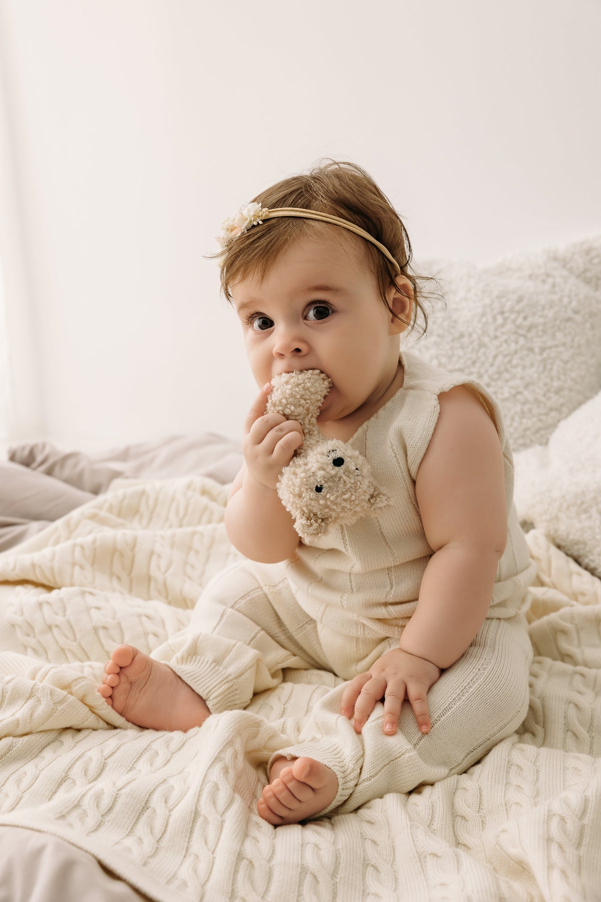 Baby in a cream outfit holding a plush toy on a braided Merino wool baby blanket.
